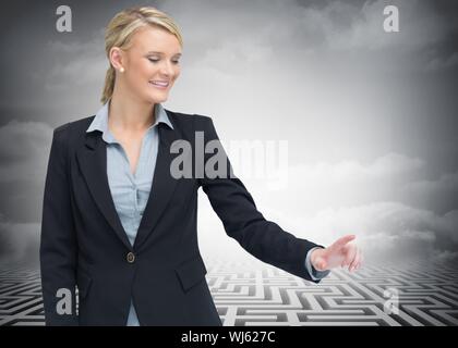 Das zusammengesetzte Bild von lächelnden Geschäftsfrau zeigen etwas, die vor riesigen Labyrinth im Hintergrund Stockfoto