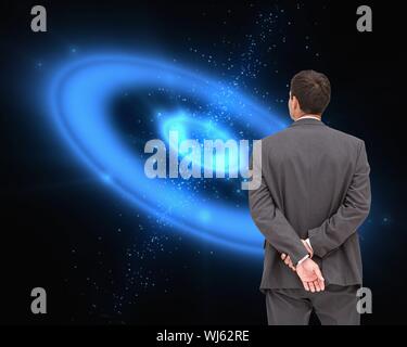 Das zusammengesetzte Bild der Geschäftsmann, der mit den Händen hinter dem Rücken vor der blauen Galaxie Hintergrund Stockfoto