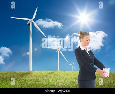 Das zusammengesetzte Bild des Blonden Geschäftsfrau Holding rosa Sparschwein stehend auf Windmühle, Feld Stockfoto