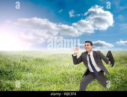 Das zusammengesetzte Bild von freudiger Geschäftsmann mit einem Koffer und läuft im Gras Stockfoto