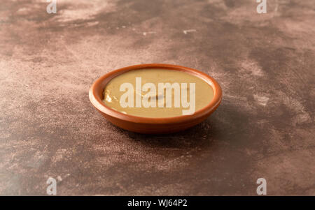 Seitenansicht der organischen Cashew-nuss Butter in einer kleinen Schüssel auf ein fleckiges maroon Tabelle mit natürlicher Beleuchtung. Stockfoto