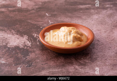 Seitenansicht des Bio Sonnenblumenöl Butter in einer kleinen Schüssel auf ein fleckiges maroon Tabelle mit natürlicher Beleuchtung. Stockfoto