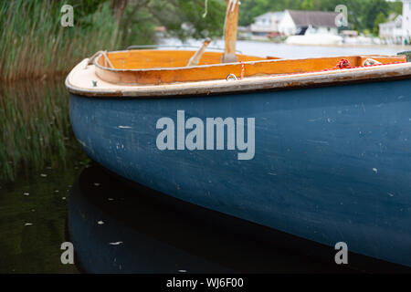 In der Nähe auf einem kleinen Segelboot mit einem blauen Rumpf schwimmend auf einer Wasserstraße mit Häusern im Hintergrund. Stockfoto