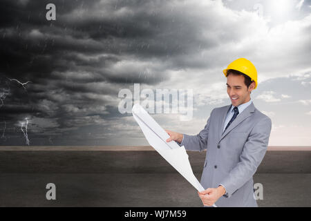 Zusammengesetztes Bild des lächelnden Architekten mit Schutzhelm, die Pläne zu betrachten Stockfoto