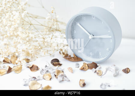 Klassische Wecker, Blumen und Blüten auf einem weißen Tisch. Gemütliche Winter oder Herbst Hintergrund Stockfoto