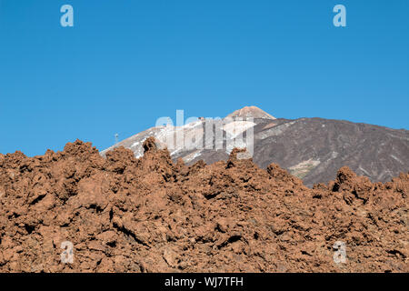 Hellbraune Farbe einer Wand aus scharfen Lavasteinen. Im Hintergrund die Berge und der Gipfel des Pico del Teide. Strahlend blauen Himmel. Teneriffa ist Stockfoto