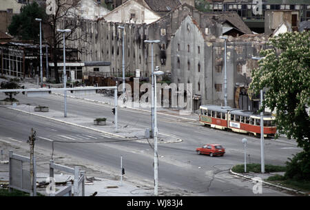 13. Mai 1993 während der Belagerung von Sarajevo: vom Holiday Inn Hotel, ein Auto, die niper Alley", Geschwindigkeiten Vergangenheit eine verbrannte Tabak Fabrik und eine verlassene Straßenbahn gesehen. Stockfoto