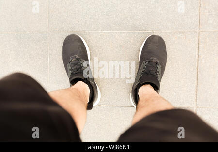 Blick von oben auf die Beine in schwarzen Sneakers auf Betonboden Stockfoto