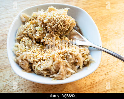 Französische Küche - Gabel in frisch geriebenen kohlrabi Salat mit Sesam und Abrichten von Honig, Balsamico und Olivenöl close-up aus weisser Keramik Stockfoto