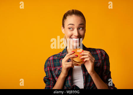 Junge Dame Essen Hamburger auf gelbem Hintergrund Stockfoto