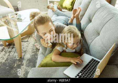 Weiblichen kaukasischen Lehrer und kleine Mädchen, oder Mutter und Tochter. Homeschooling. Auf dem Sofa und mit Laptop für Kenntnisse erhalten während der Lektion ist. Bildung, Schule, Studium Konzept. Stockfoto