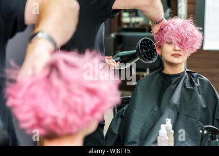 Professionelle Friseur trocknet das Haar mit einem Haartrockner in Spiegelbild Stockfoto