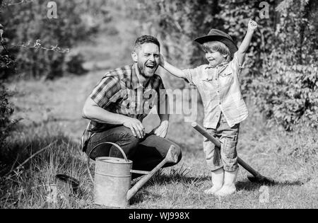 Bewässerung von Pflanzen. happy Earth Day. Stammbaum nursering. Vater und Sohn in Cowboy Hut auf Ranch. kleiner Junge Kind helfen Vater in der Landwirtschaft. Gießkanne, Topf und Schaufel. Gartengeräte. Eco Farm. Stockfoto