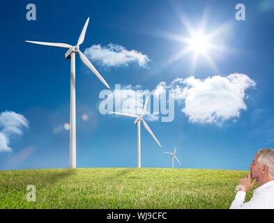 Das zusammengesetzte Bild von nachdenklich reife Geschäftsmann am Windmühle stehend auf Gras unter sonnigen Himmel Stockfoto