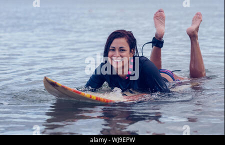 Porträt eines lächelnden Frau schwimmen über Surfbrett im Wasser am Strand Stockfoto