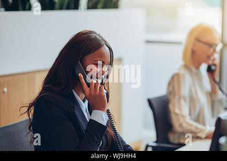 Afrikanische amerikanische Geschäftsfrau Gespräch am Telefon und lachend, während bei einem Büro Rezeption mit einem Kollegen arbeiten Stockfoto