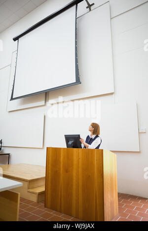 Elegante Lehrerin mit Computer und Projektionsfläche im Hörsaal Stockfoto