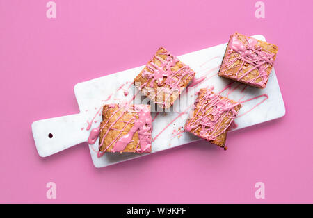 Ruby chocolate Brownies auf Marmor Schneidbrett und rosa Hintergrund. Oben Ansicht von rosa Schokolade Dessert. Flach von ruby Schokolade Süßigkeiten. Stockfoto