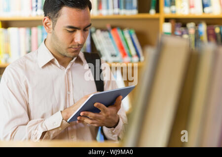 Ältere Teilnehmer mit Tablet-PC gegen Regal in der Bibliothek konzentriert Stockfoto