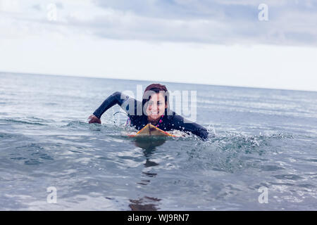 Porträt eines lächelnden Frau schwimmen über Surfbrett im Wasser am Strand Stockfoto