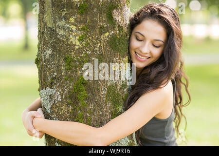 Lässige fröhliche brunette, einen Baum mit geschlossenen Augen in einem Park an einem sonnigen Tag Stockfoto