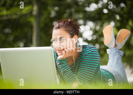 Nachdenklich and student auf Gras liegend mit Laptop auf dem Campus an der Hochschule Stockfoto