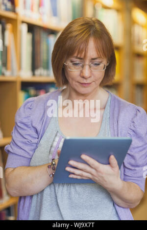 Weibliche Bibliothekar mit konzentrierten ihre Tabletten stehen in einer Bibliothek Stockfoto