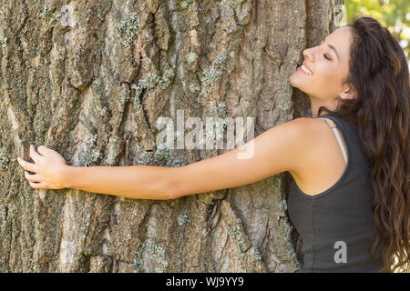 Casual Inhalt brunette, einen Baum mit geschlossenen Augen in einem Park an einem sonnigen Tag Stockfoto