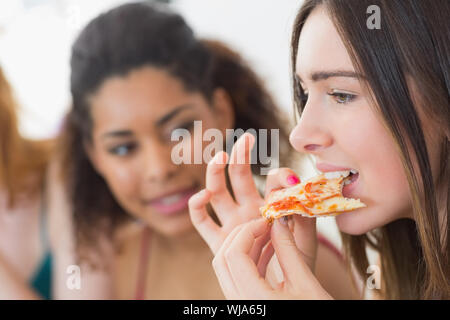 Nahaufnahme eines jungen weiblichen essen Pizza mit unscharfen Freunde zu Hause Stockfoto