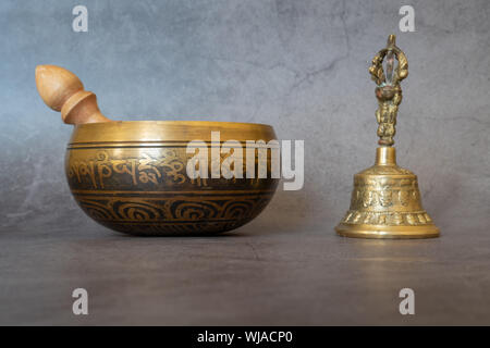 Klangschalen und Golden Bell close-up, beruhigend und meditativ. Klangschale mit Sanskrit Gravur Muster und Holzhammer und Golden Bell der auf g Stockfoto