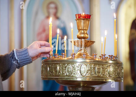 Die Hand eines Mannes stellt eine Kerze vor dem Symbol der Russischen Orthodoxen Kirche Stockfoto