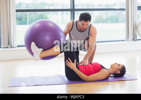 Trainer helfen junge Frau mit Fitness-Ball in Turnhalle Stockfoto