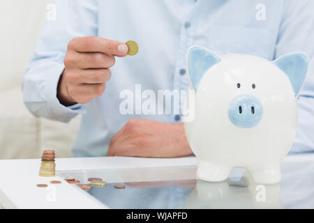 Mittelteil eines Mannes setzen einige Münzen in ein Sparschwein Stockfoto