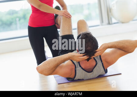 Weibliche Trainer unterstützen Mann mit seinen Übungen im Fitness-Studio Stockfoto