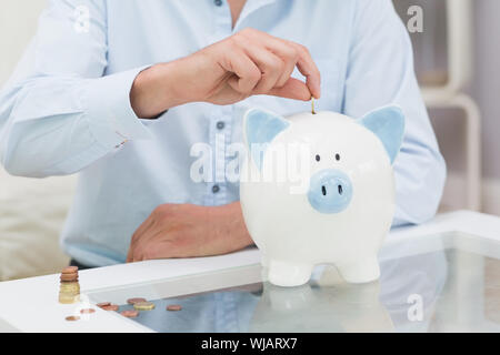 Mittelteil eines Mannes setzen einige Münzen in ein Sparschwein Stockfoto