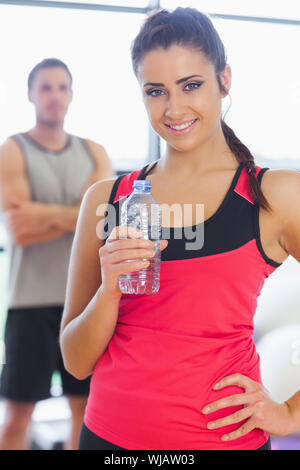 Fit Frau mit Wasserflasche mit Freund im Hintergrund im Fitnessraum Stockfoto