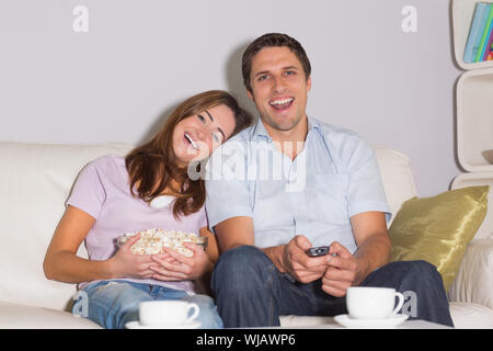 Fröhliches paar vor dem Fernseher mit Popcorn Schüssel zu Hause auf sofa Stockfoto