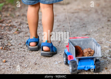 Rückansicht des unteren Abschnitt von einem 3-4 jährigen Kind in kurzen Hosen im Sommer Ziehen einer Spielzeug-LKW mit Kegel in Es Stockfoto