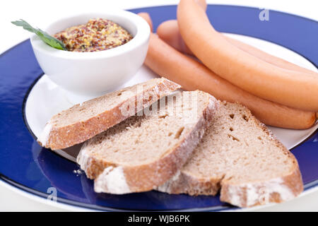 Drei kalt geräucherte Würstchen oder Wiener Würstchen serviert auf einem Teller mit einem Sprung in eine kleine Schüssel geben und in Scheiben geschnittenen Kirschtomaten auf ein weißes Studio-Hintergrund Stockfoto