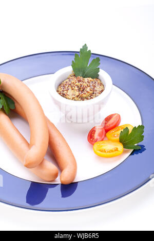 Drei kalt geräucherte Würstchen oder Wiener Würstchen serviert auf einem Teller mit einem Sprung in eine kleine Schüssel geben und in Scheiben geschnittenen Kirschtomaten auf ein weißes Studio-Hintergrund Stockfoto