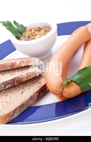 Drei kalt geräucherte Würstchen oder Wiener Würstchen serviert auf einem Teller mit einem Sprung in eine kleine Schüssel geben und in Scheiben geschnittenen Kirschtomaten auf ein weißes Studio-Hintergrund Stockfoto