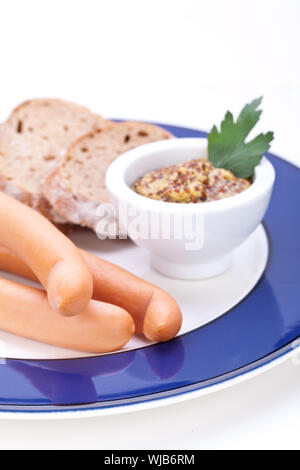 Drei kalt geräucherte Würstchen oder Wiener Würstchen serviert auf einem Teller mit einem Sprung in eine kleine Schüssel geben und in Scheiben geschnittenen Kirschtomaten auf ein weißes Studio-Hintergrund Stockfoto
