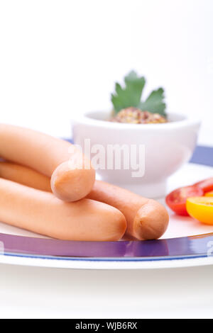 Drei kalt geräucherte Würstchen oder Wiener Würstchen serviert auf einem Teller mit einem Sprung in eine kleine Schüssel geben und in Scheiben geschnittenen Kirschtomaten auf ein weißes Studio-Hintergrund Stockfoto
