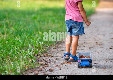 Rückansicht des unteren Abschnitt von einem 3-4 jährigen Kind in kurzen Hosen im Sommer Ziehen einer Spielzeug-LKW mit Kegel in Es Stockfoto