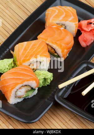 Anordnung der Philadelphia Sushi mit Wasabi, mariniertem Ingwer und Sojasauce in Schwarz quadratische Form Schüsseln mit Paar Essstäbchen auf Stroh matte backgro Stockfoto