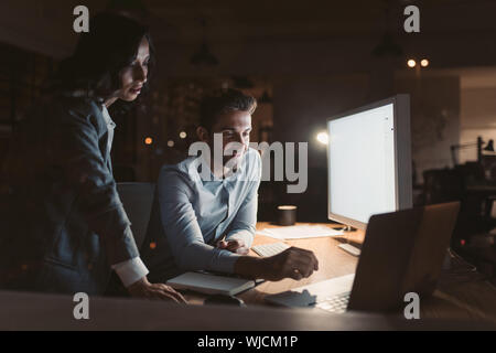 Lächelnd Arbeitskollegen auf einem Computer zusammen arbeiten bei Nacht Stockfoto
