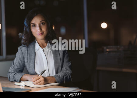 Junge Geschäftsfrau, Lächeln, während sie in ihrem Büro in der Nacht arbeiten Stockfoto