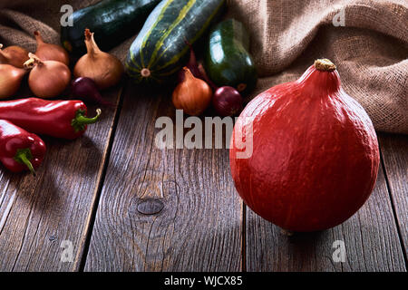 Stillleben mit orange Kürbis, Paprika und Zwiebeln. Grüne Zucchini liegt auf einem alten Holztisch. Stockfoto