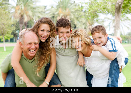 Granparents Schweinchen-Fahrt für junge Generation geben, wie sie in die Kamera Lächeln Stockfoto