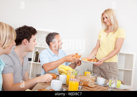 Junge gesunde Familie am Tisch serviert von der lächelnden Mutter Croissants zum Frühstück Stockfoto